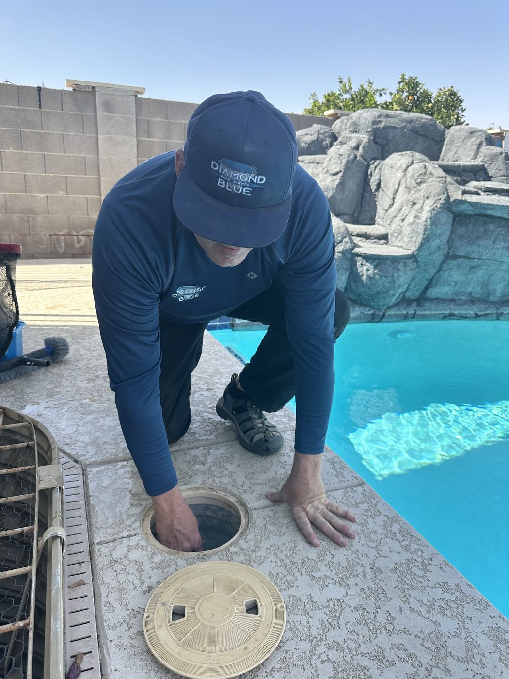 Diamond Blue Pool Service technician cleaning the skimmer basket and checking equipment