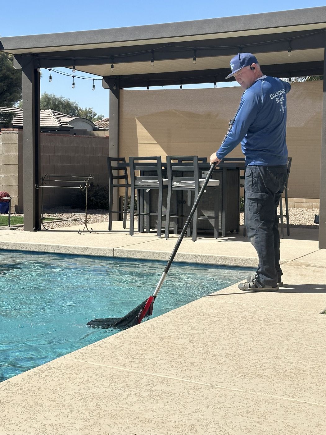 Diamond Blue Pool Service technician skimming a pool with a net in Queen Creek AZ
